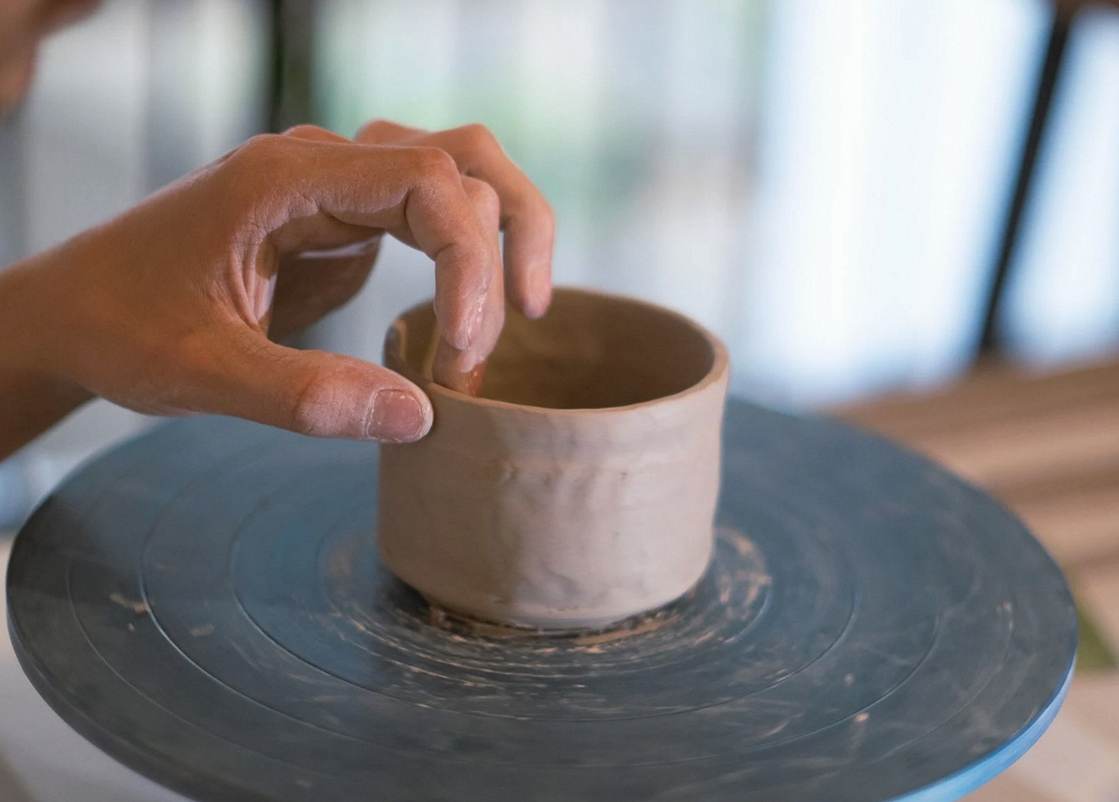 陶芸ろくろで粘土の壺を成形する手のクローズアップ。職人的な制作過程を強調。